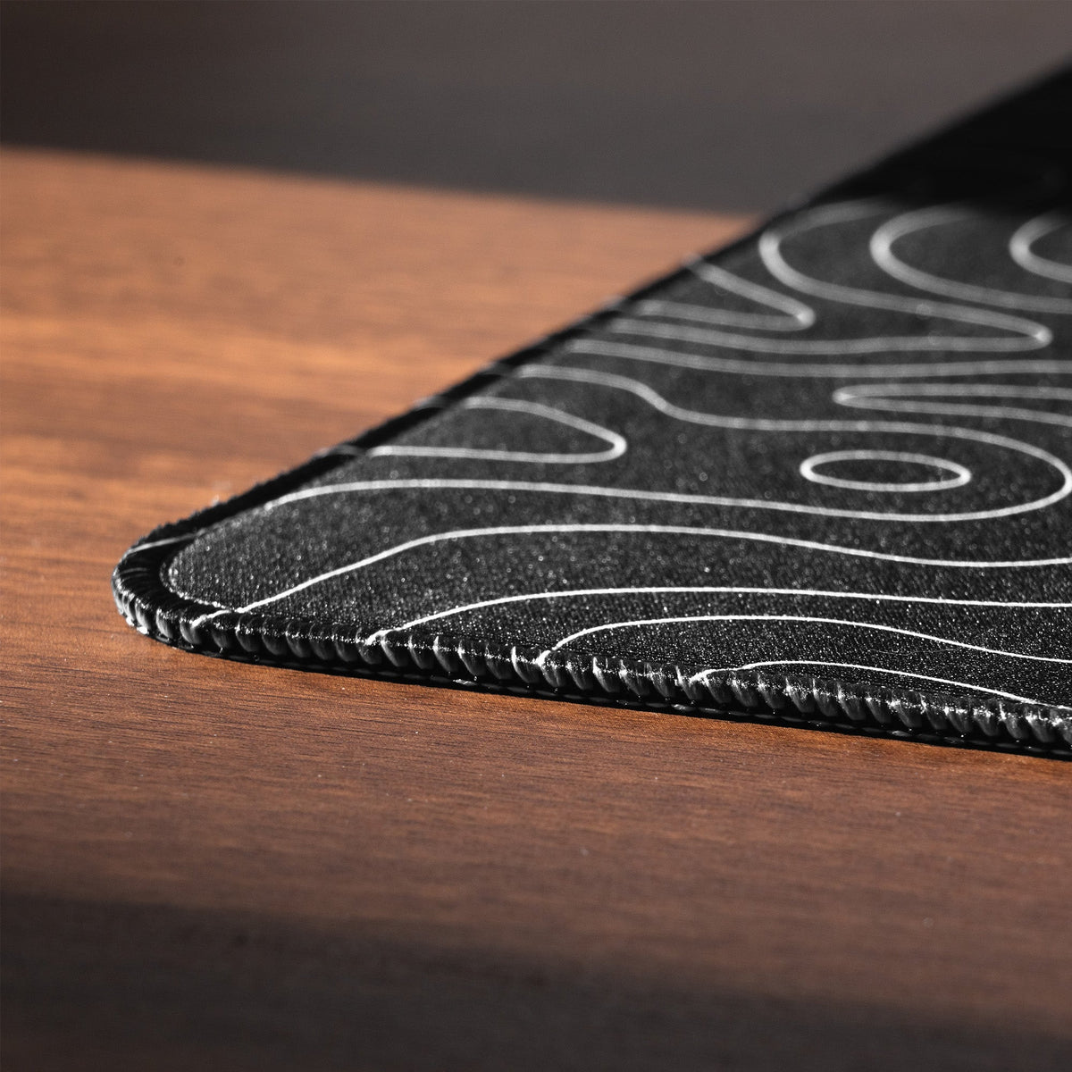 Stitched edge of an XVX Topographic desk mat resting on a desk